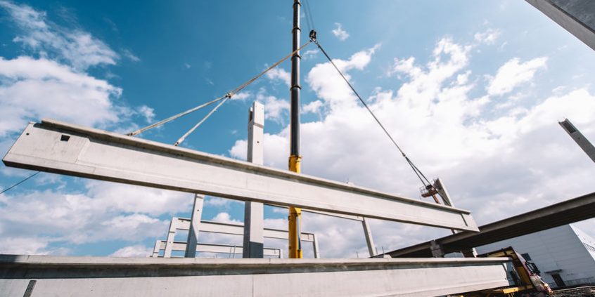 Industrial heavy duty crane lifting precast cement beams and pillars on construction site